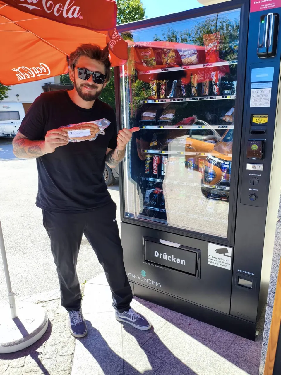 Getränkeautomat von Flo's Getränke Service bei der Metzgerei Wopfner in Kundl – ein Kunde zeigt die frisch gezogene Käsekrainer